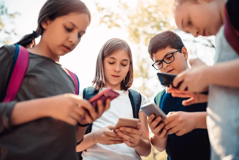 Zdjęcie przedstawia grupkę dzieci patrzących w ekran swojego telefonu